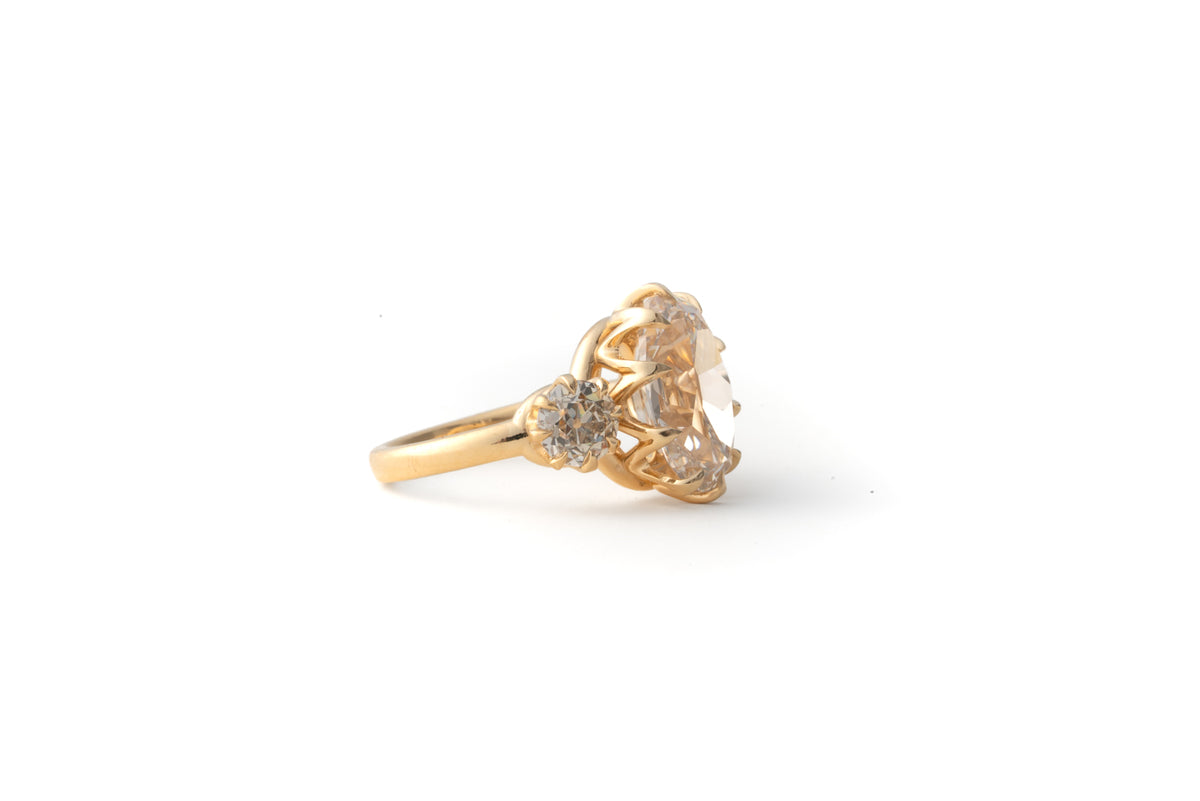 A yellow gold ring featuring a large, round, pale-colored center stone and a smaller side diamond, set against a plain white background.