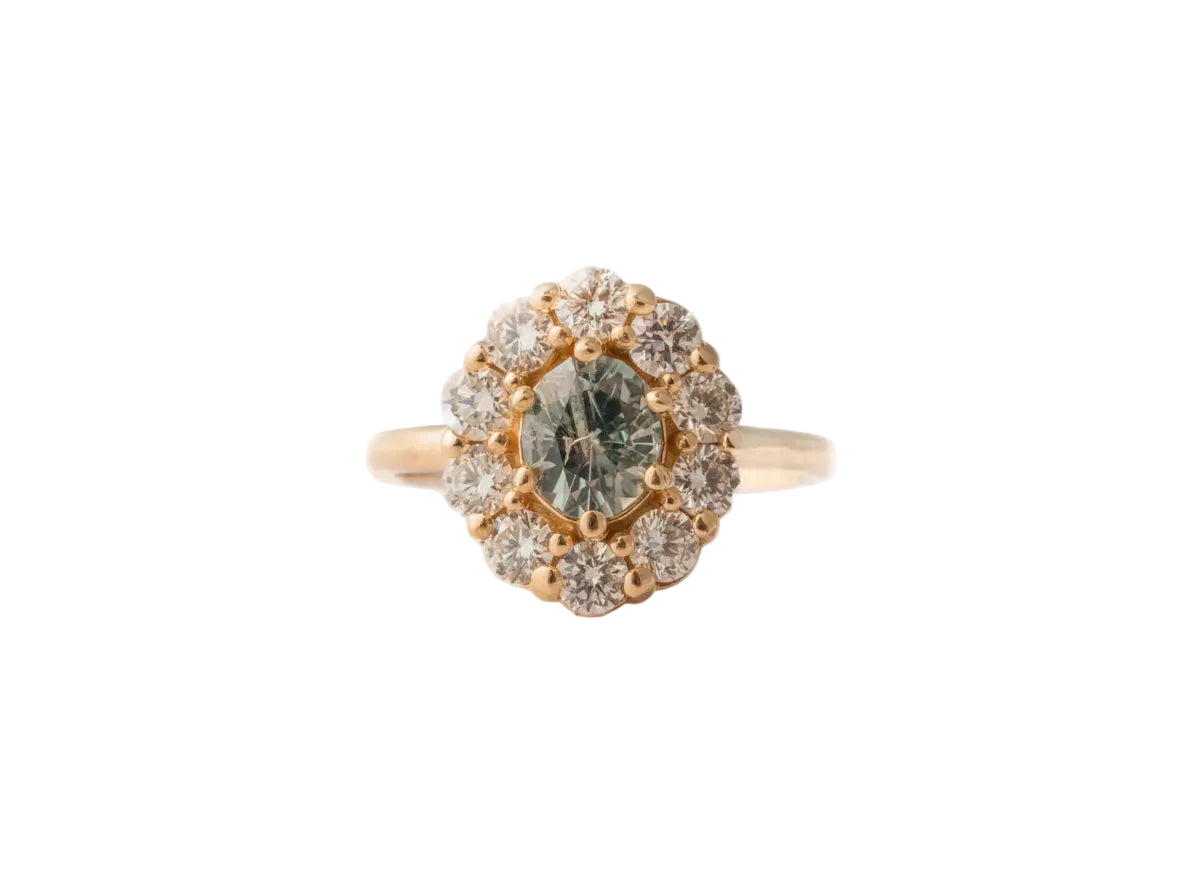 Gold ring with a central green gemstone and diamond-studded halo on a white background