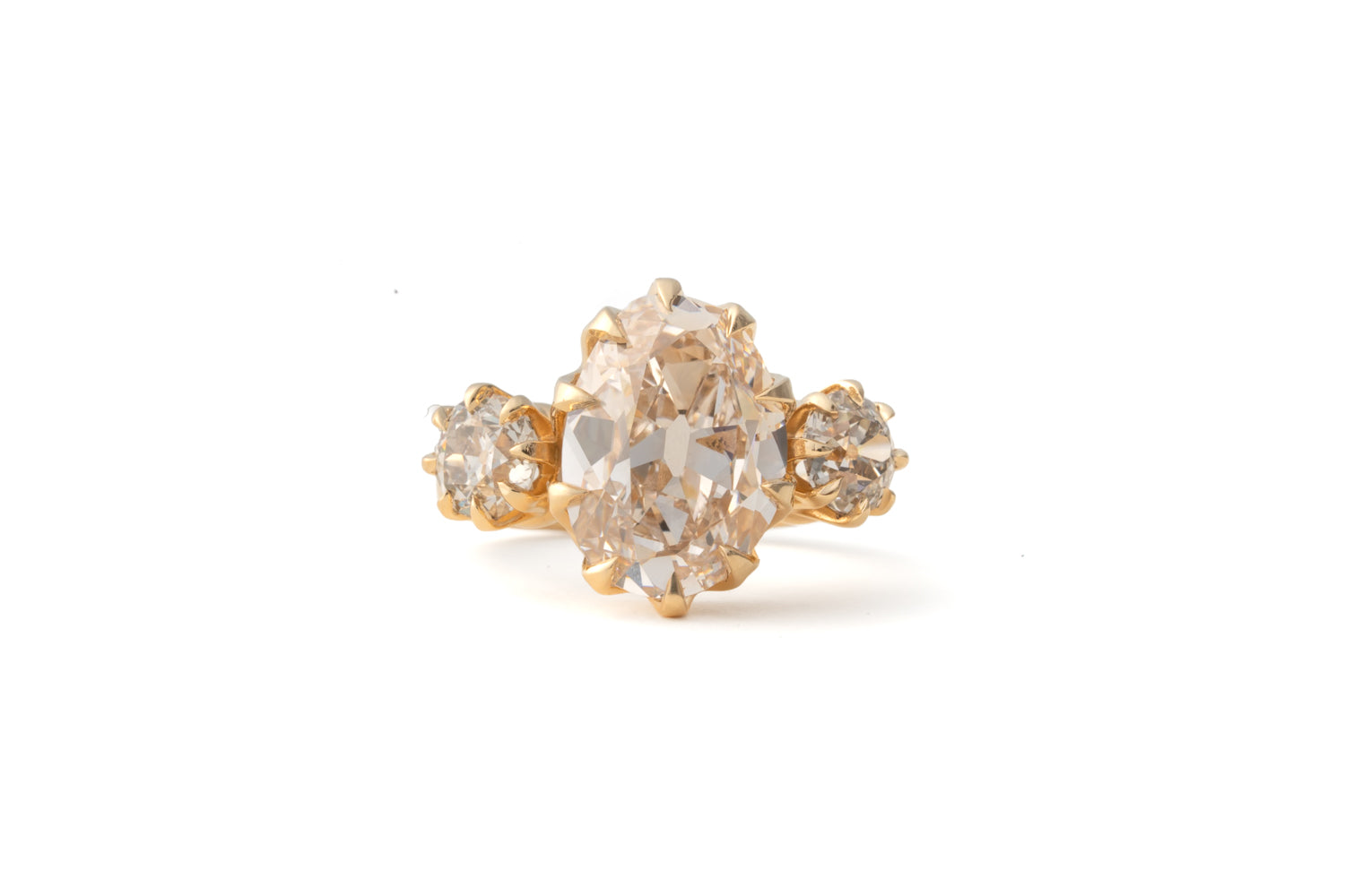 A vintage-style gold ring featuring a large oval pale pinkish gemstone in the center, flanked by two smaller round clear stones on a white background.