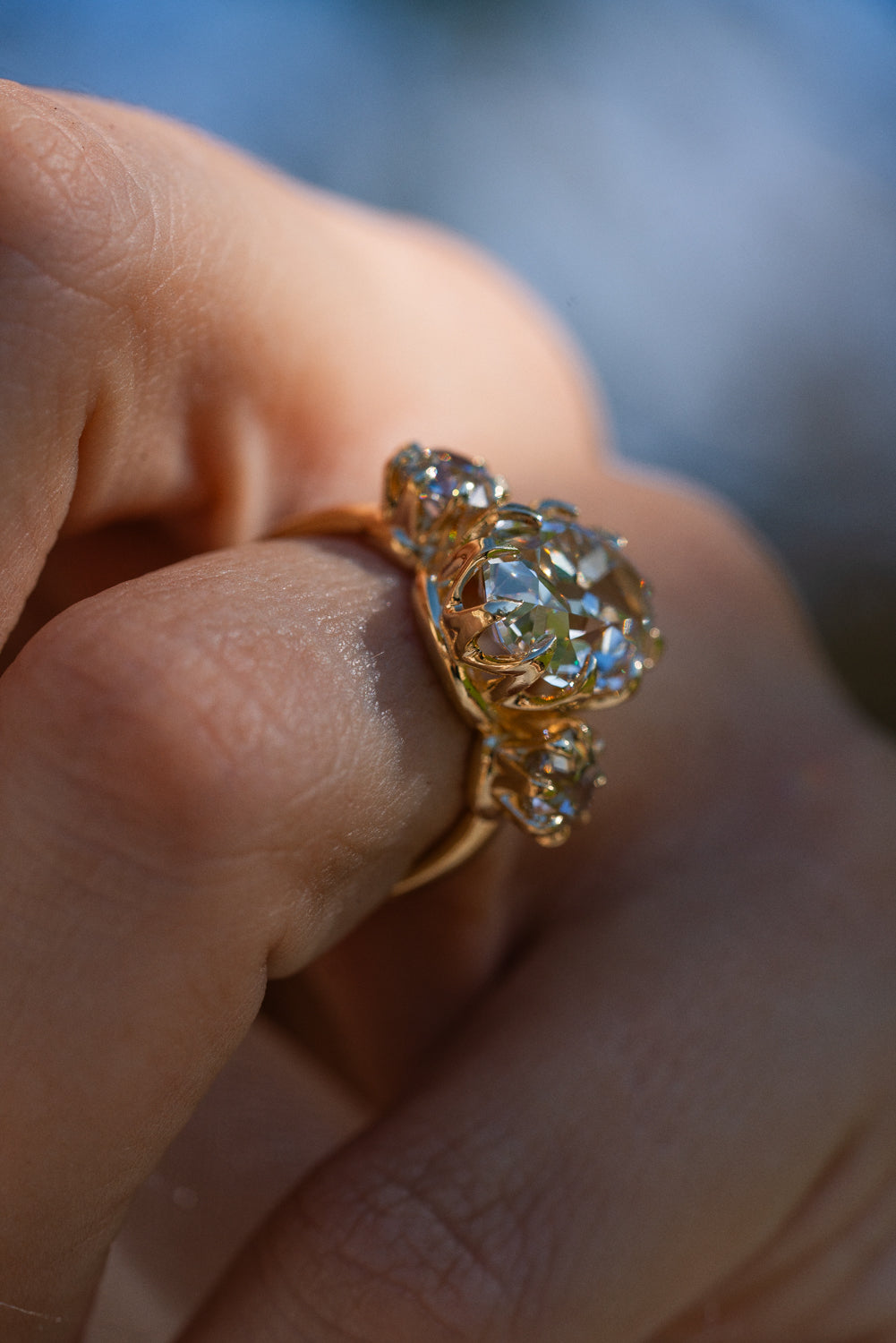 A close-up of a hand wearing a vintage gold ring with a large floral cluster of clear round-cut diamonds.